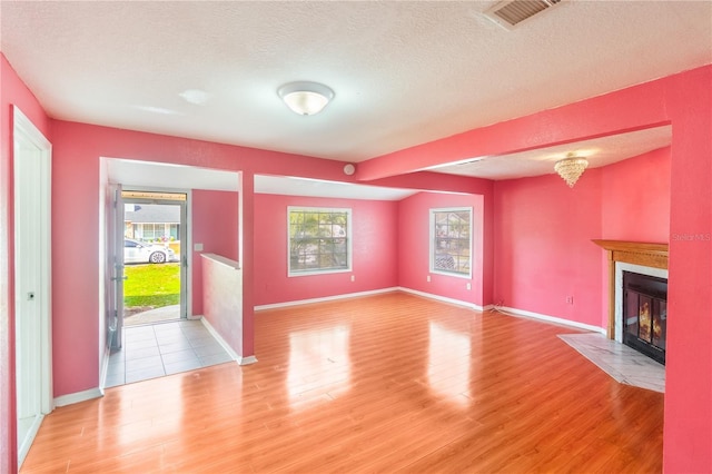 unfurnished living room with a fireplace with flush hearth, light wood-style floors, plenty of natural light, and a textured ceiling