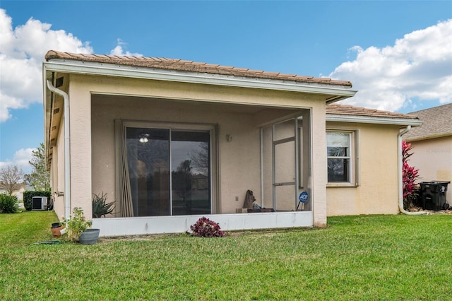 rear view of house featuring stucco siding, central AC unit, a yard, and a sunroom