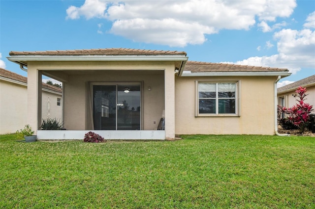 back of property featuring a tiled roof, a lawn, a sunroom, and stucco siding