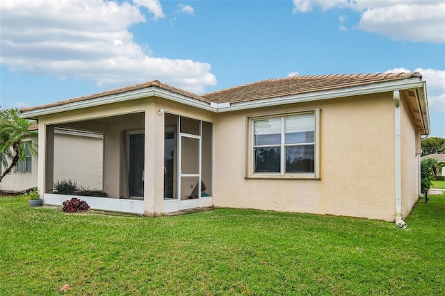 rear view of property featuring stucco siding, a lawn, and a sunroom