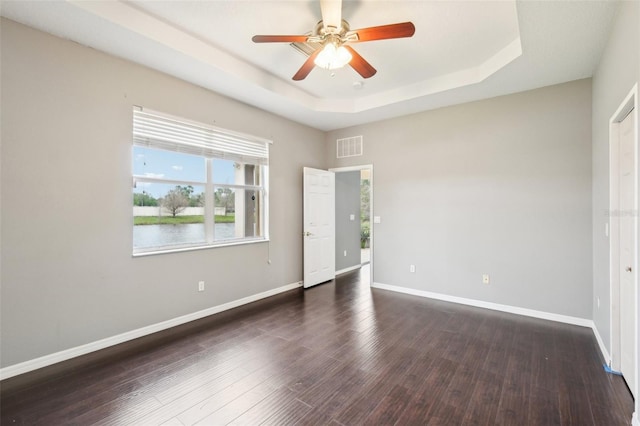 spare room featuring dark wood finished floors, visible vents, a raised ceiling, and baseboards