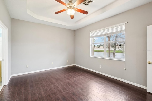 spare room with dark wood finished floors, a tray ceiling, visible vents, and baseboards