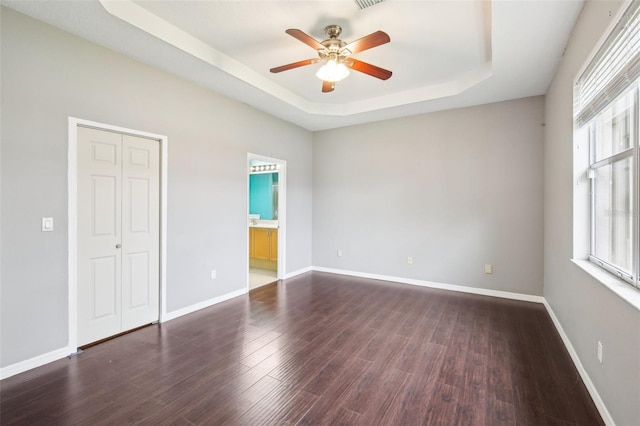 unfurnished bedroom with a ceiling fan, dark wood-style floors, baseboards, a closet, and a raised ceiling