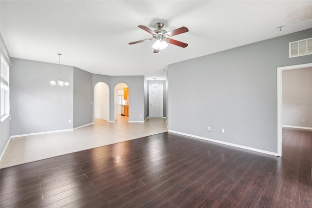 empty room with arched walkways, visible vents, baseboards, and wood finished floors