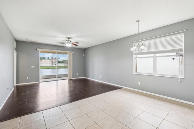 empty room with ceiling fan with notable chandelier, light wood-style floors, and baseboards