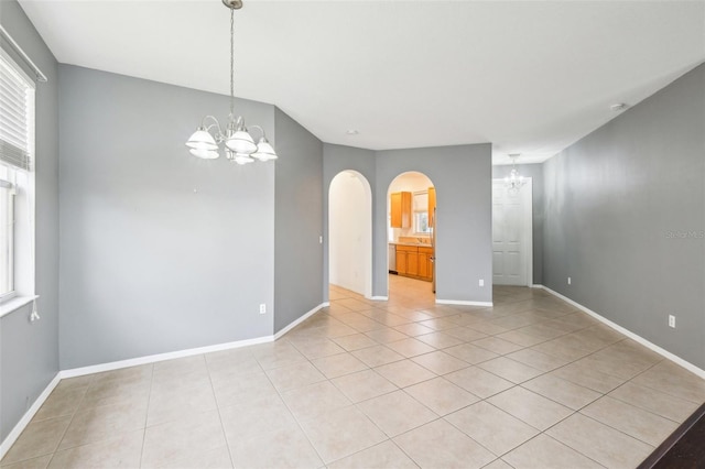 unfurnished room with light tile patterned floors, baseboards, a notable chandelier, and arched walkways