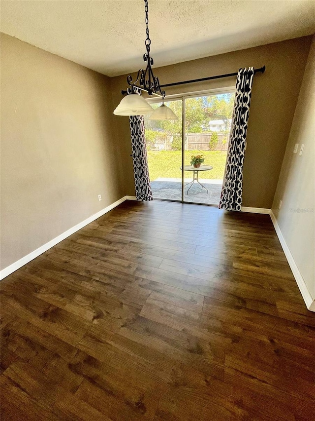 unfurnished dining area featuring dark wood-type flooring, baseboards, and a textured ceiling