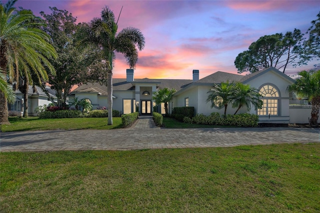 view of front of home with french doors, a chimney, a front lawn, and stucco siding