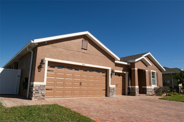 view of front facade with stone siding, stucco siding, an attached garage, and decorative driveway