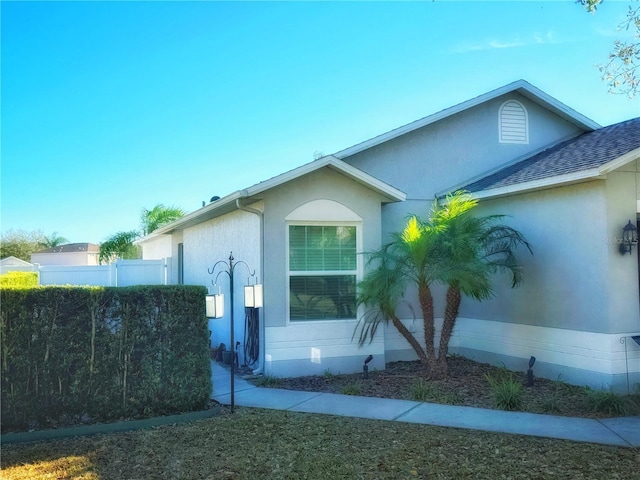 view of property exterior with roof with shingles, fence, and stucco siding