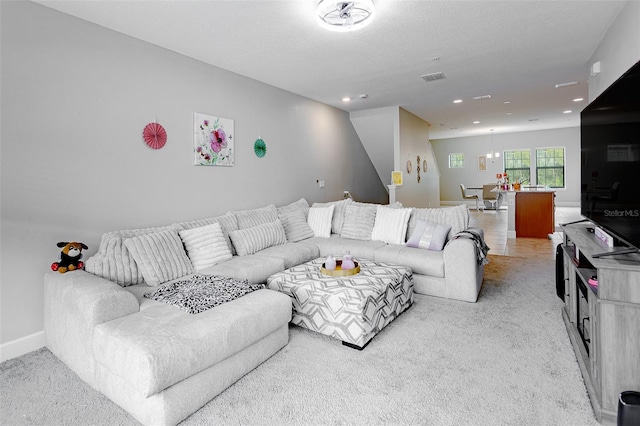 living room featuring light colored carpet, visible vents, a textured ceiling, and baseboards