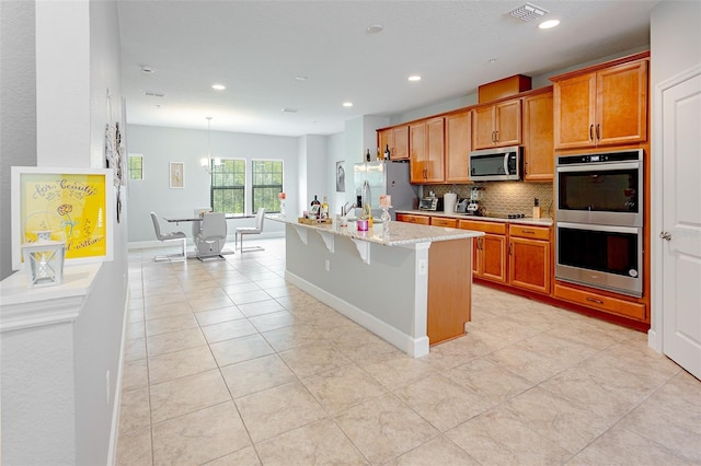 kitchen featuring appliances with stainless steel finishes, brown cabinetry, visible vents, and a center island with sink