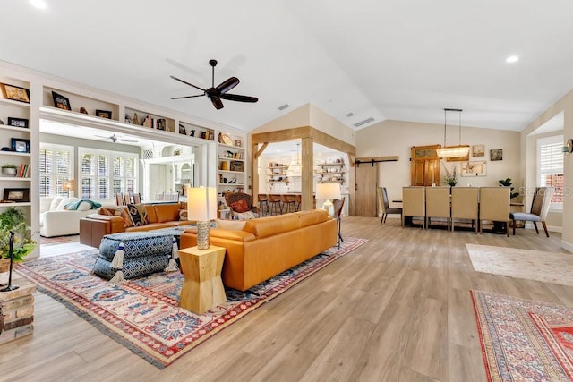 living room featuring light wood-type flooring, built in shelves, a barn door, lofted ceiling, and ceiling fan