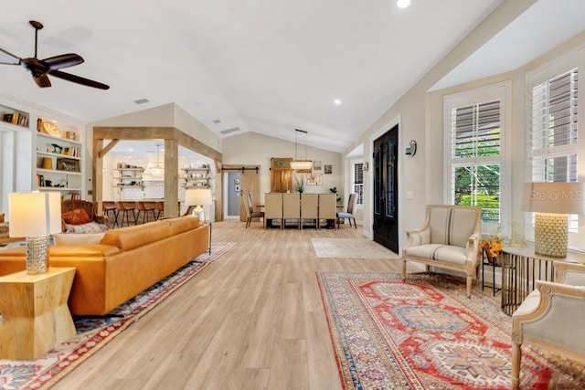 living room with built in shelves, a ceiling fan, wood finished floors, vaulted ceiling, and a barn door