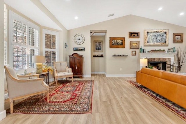 sitting room featuring visible vents, light wood-style flooring, baseboards, a fireplace, and lofted ceiling