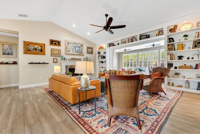 living area featuring light wood finished floors, visible vents, a brick fireplace, built in shelves, and vaulted ceiling