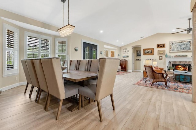 dining area with lofted ceiling, a fireplace, light wood finished floors, baseboards, and ceiling fan