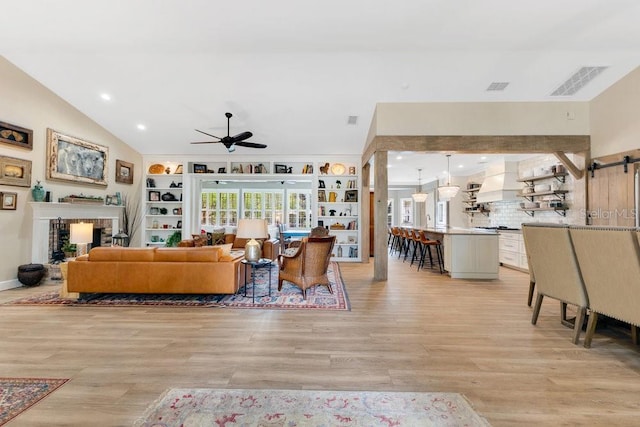 living room with ceiling fan, visible vents, light wood-style flooring, and vaulted ceiling