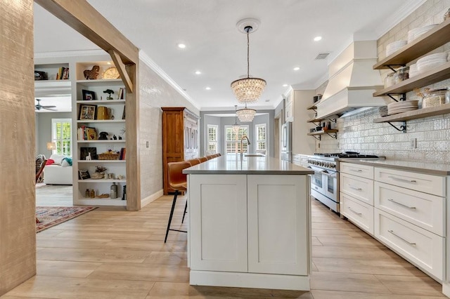 kitchen with light wood-type flooring, a kitchen bar, high end stove, open shelves, and a sink