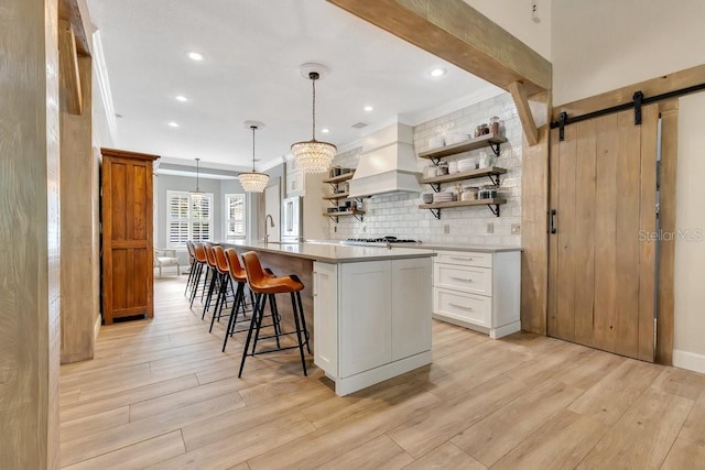 kitchen with custom range hood, open shelves, backsplash, a barn door, and light countertops