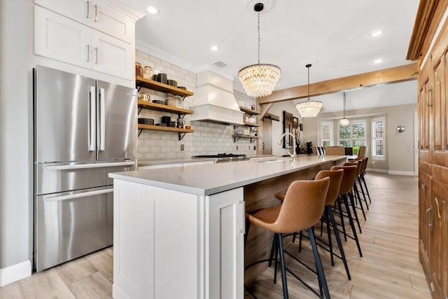 kitchen featuring open shelves, freestanding refrigerator, a sink, light countertops, and custom range hood