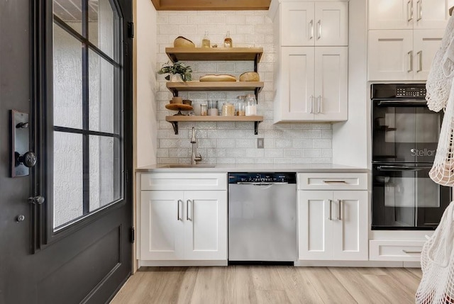 kitchen with dishwasher, light countertops, light wood-style floors, dobule oven black, and a sink