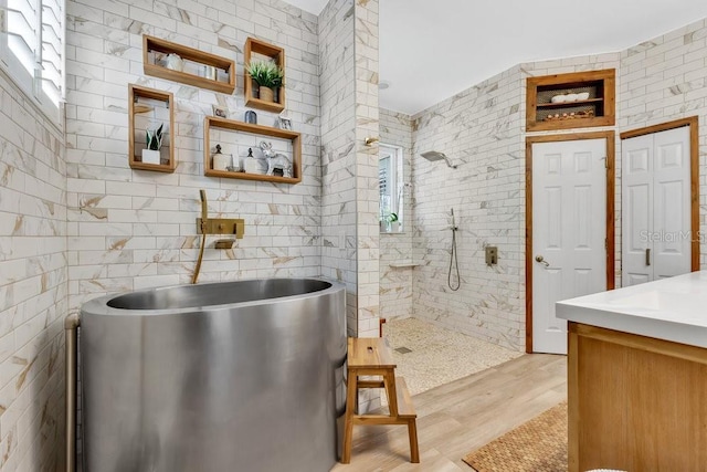 full bathroom featuring walk in shower, wood finished floors, vanity, a freestanding tub, and tile walls