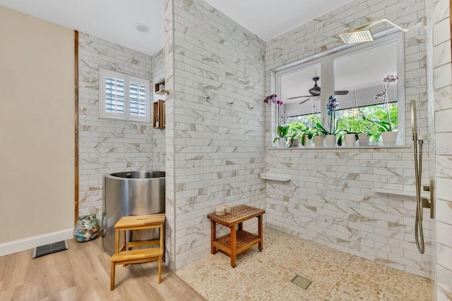 bathroom featuring wood finished floors, baseboards, visible vents, tiled shower, and ceiling fan