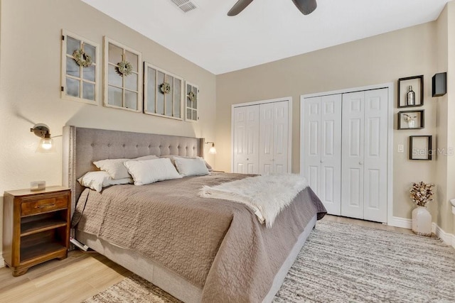 bedroom with baseboards, light wood finished floors, visible vents, ceiling fan, and two closets