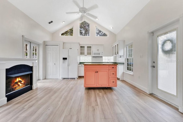 kitchen with visible vents, light wood-type flooring, a glass covered fireplace, white appliances, and high vaulted ceiling