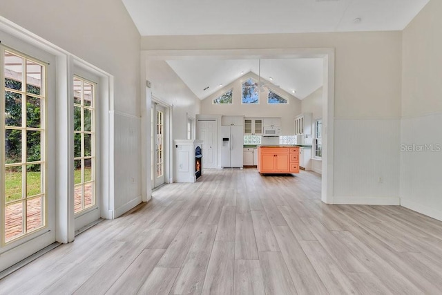 unfurnished living room with light wood-style flooring, high vaulted ceiling, and wainscoting