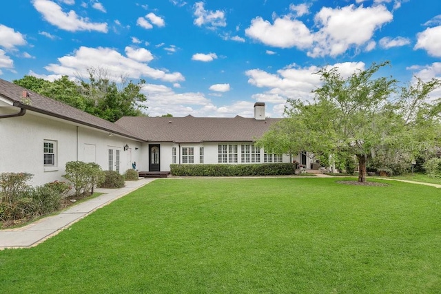 rear view of house featuring stucco siding, a lawn, and a chimney