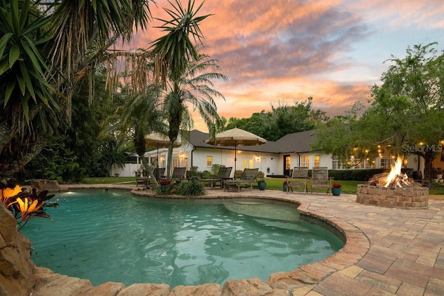 pool at dusk with a fenced in pool, a fire pit, and a patio