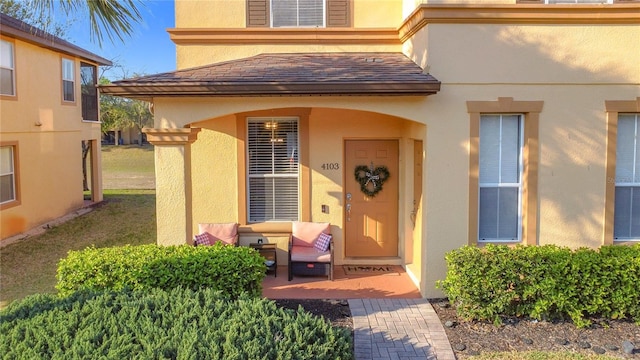 entrance to property featuring a shingled roof and stucco siding