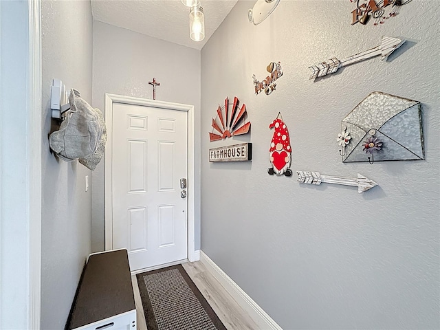 doorway with a textured ceiling, wood finished floors, and baseboards