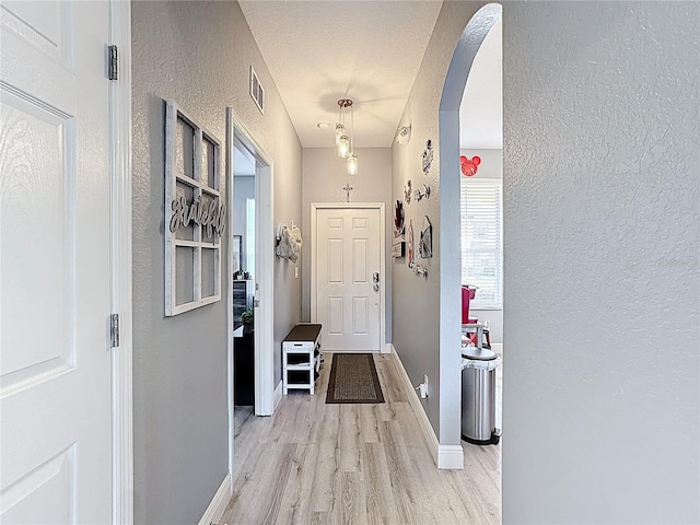 interior space with arched walkways, a textured wall, visible vents, baseboards, and light wood finished floors