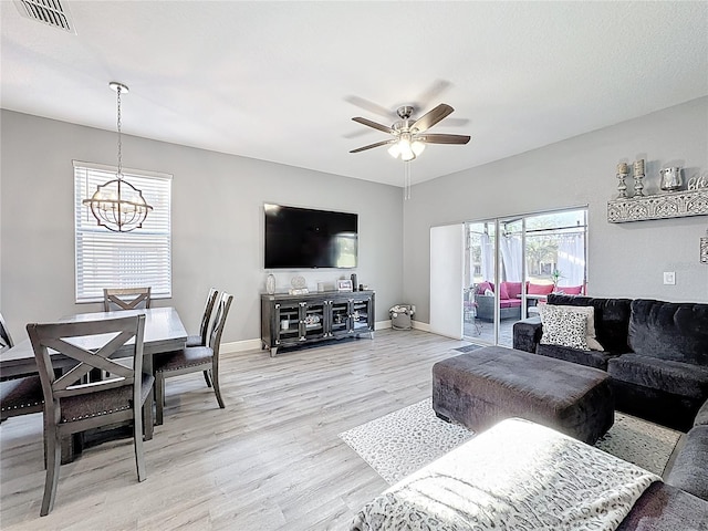 living room with light wood-type flooring, visible vents, baseboards, and ceiling fan with notable chandelier