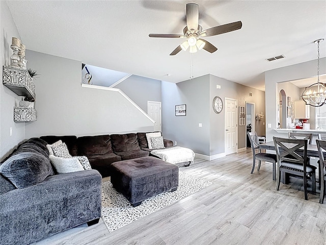 living room with light wood-type flooring, visible vents, baseboards, and ceiling fan with notable chandelier