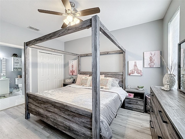 bedroom featuring light wood-style floors, ensuite bath, visible vents, and a closet