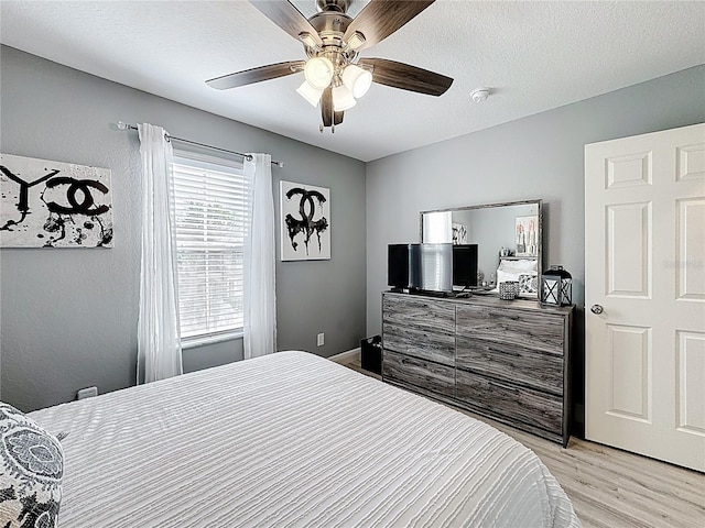 bedroom with a textured ceiling, a ceiling fan, and light wood-style floors