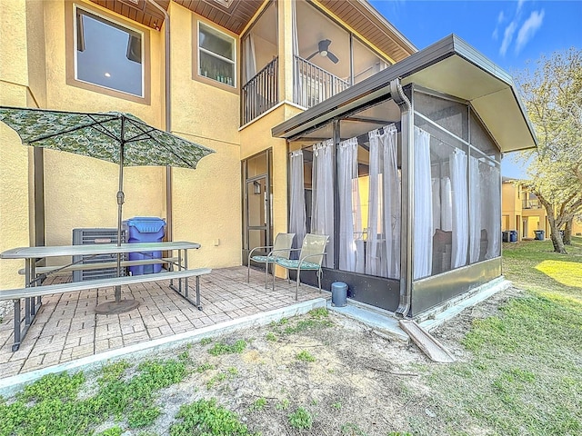 rear view of house featuring a sunroom, a patio, and stucco siding