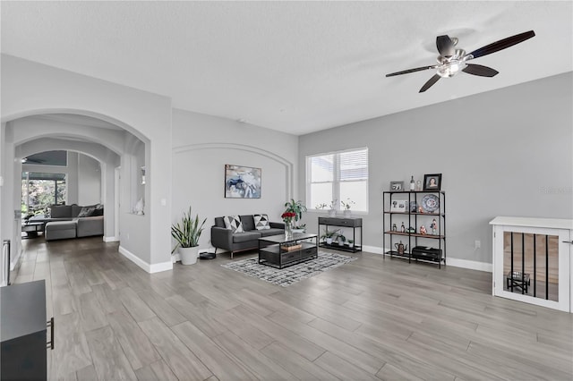 living area with a wealth of natural light, arched walkways, light wood-style floors, and a textured ceiling