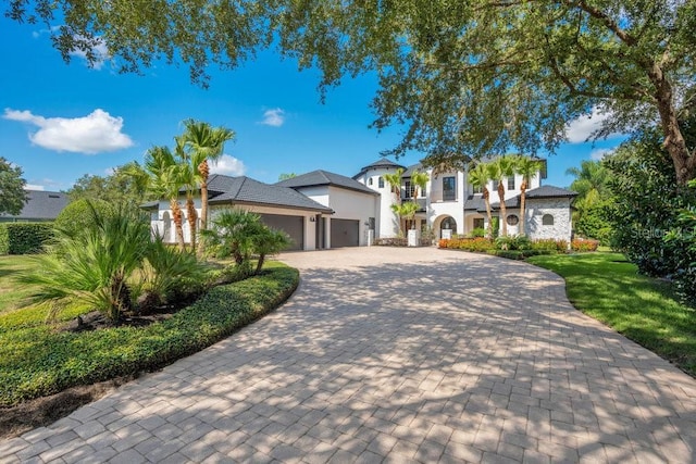 mediterranean / spanish-style house featuring an attached garage, stucco siding, a front lawn, stone siding, and decorative driveway