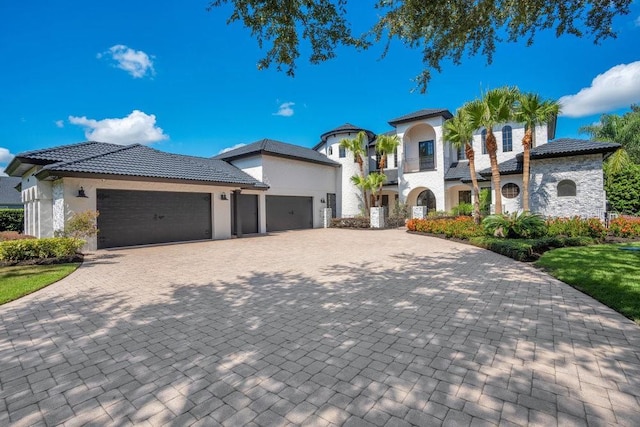 mediterranean / spanish-style house with stucco siding, a tile roof, decorative driveway, an attached garage, and a balcony