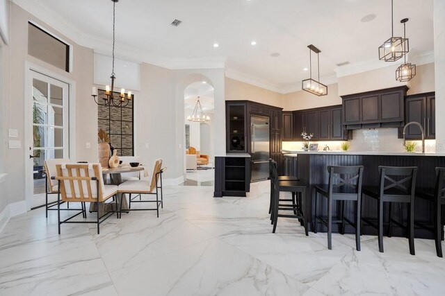 kitchen featuring decorative backsplash, built in refrigerator, a chandelier, and crown molding