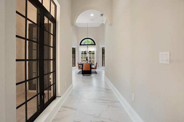 hallway with baseboards, an inviting chandelier, french doors, a towering ceiling, and marble finish floor