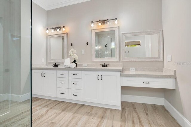 bathroom with a walk in shower, a sink, crown molding, double vanity, and baseboards