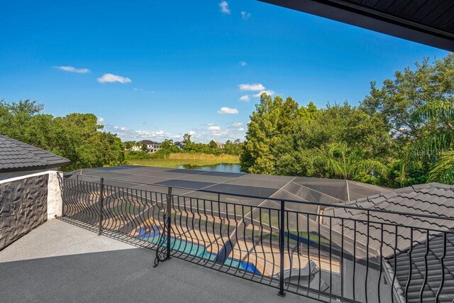 view of patio with glass enclosure, an outdoor pool, a balcony, and a water view