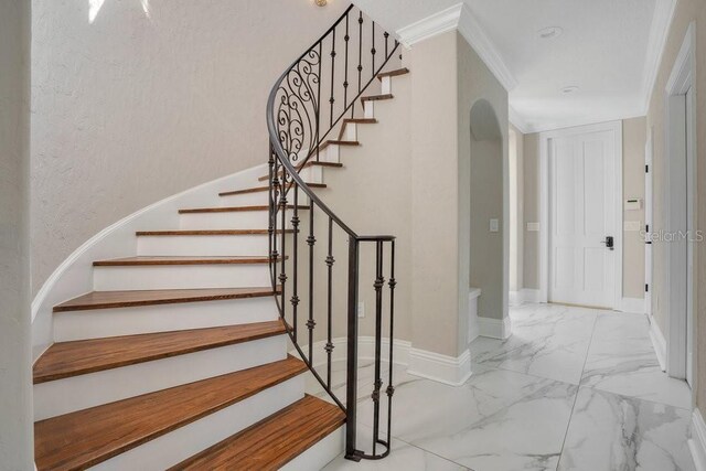 stairway with arched walkways, marble finish floor, crown molding, and baseboards