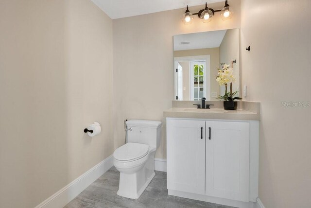 half bathroom featuring vanity, toilet, wood finished floors, and baseboards